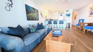 A living room with a sofa, a coffee table, and a kitchen in the background. - Seamist #6-Oceanfront-Wonderful View! (Seacrest)