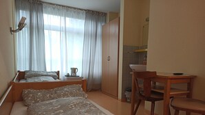 A bedroom with a bed, a bedside table, a chair, a small table with a bowl, and a kitchen area with a sink and cabinets. - Restaurant El Greco (Gundelfingen an der Donau)
