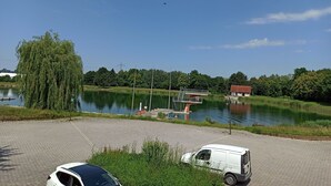 A view of a lake with a dock, a white van, and a building with a red roof. - Restaurant El Greco (Gundelfingen an der Donau)