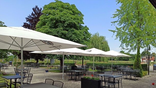 An outdoor cafe with tables and chairs under white umbrellas, surrounded by greenery and trees. - Restaurant El Greco (Gundelfingen an der Donau)