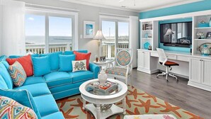 Una sala de estar con un sofá azul, una mesa de centro redonda y un televisor sobre un mueble blanco.