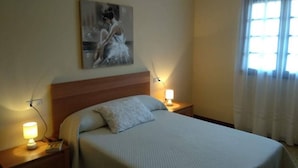 Een hotelkamer met een bed, een nachtkastje met een lamp, een schilderij aan de muur en een raam met gordijnen.