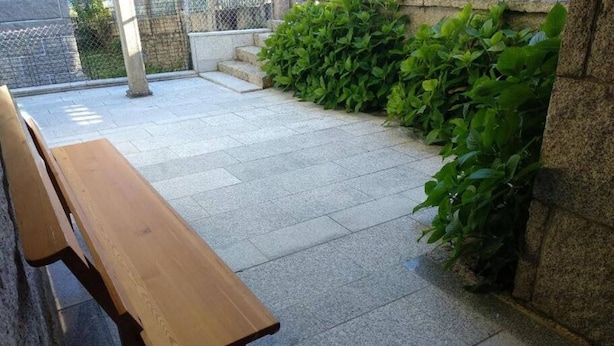 Een houten bank in een binnentuin met stenen tegels en groene planten.