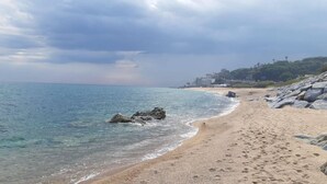 A beach with clear water, rocky outcrops, and buildings in the background.