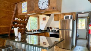 Eine moderne Küche mit einem Edelstahlkühlschrank, einer Mikrowelle und einem Wasserkocher auf dem Herd. Es gibt eine Holzauslage mit Barhocker und eine Uhr darüber.
