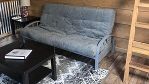 A cozy loft bedroom with a wooden ceiling, a gray sofa, a black coffee table, and a painting of a sunset over water. - Chalet with Hot Tub & Pet Friendly (Summersville)