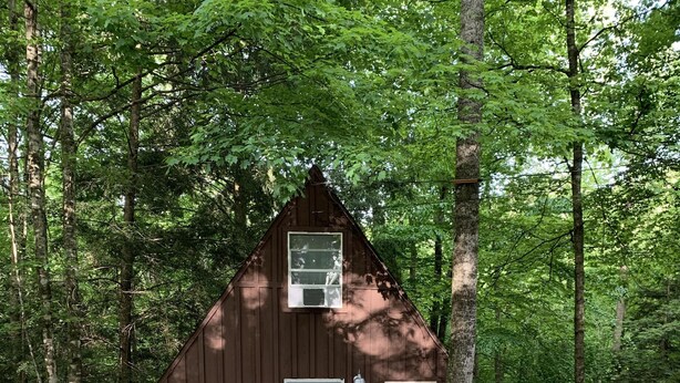 A brown wooden cabin with a white door, a small porch, and a gravel driveway surrounded by trees. - Chalet with Hot Tub & Pet Friendly (Summersville)