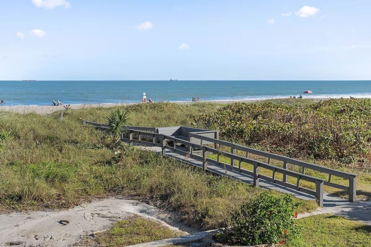 Ein Strand mit einer Holzpromenade, die zum Ufer führt, umgeben von Vegetation.