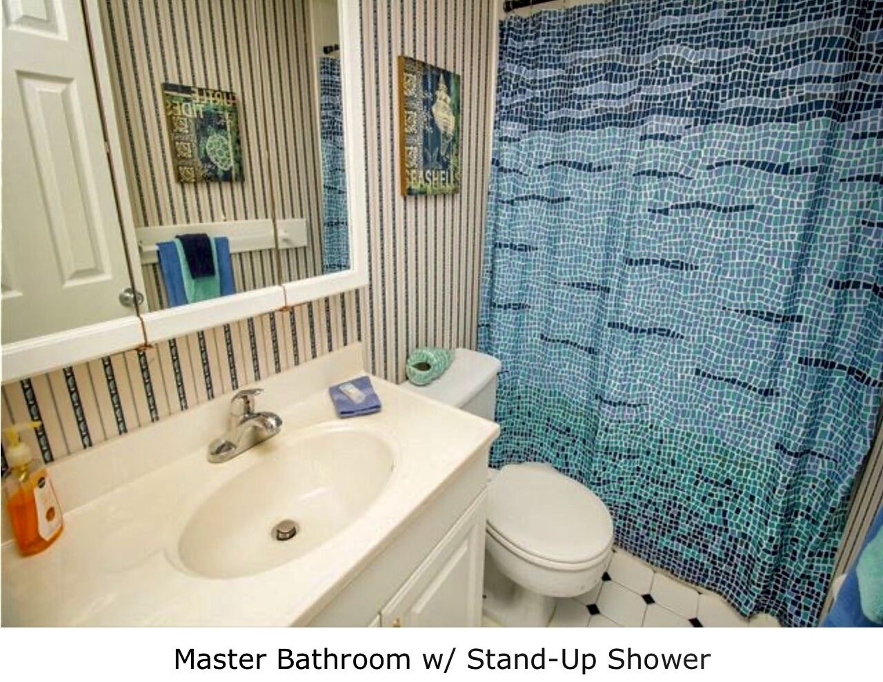 Une salle de bain principale dotée d’une douche à l’italienne, avec un mur à rayures, un lavabo blanc et des toilettes.
