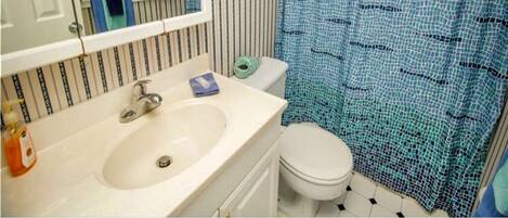 Une salle de bain principale dotée d’une douche à l’italienne, avec un mur à rayures, un lavabo blanc et des toilettes.