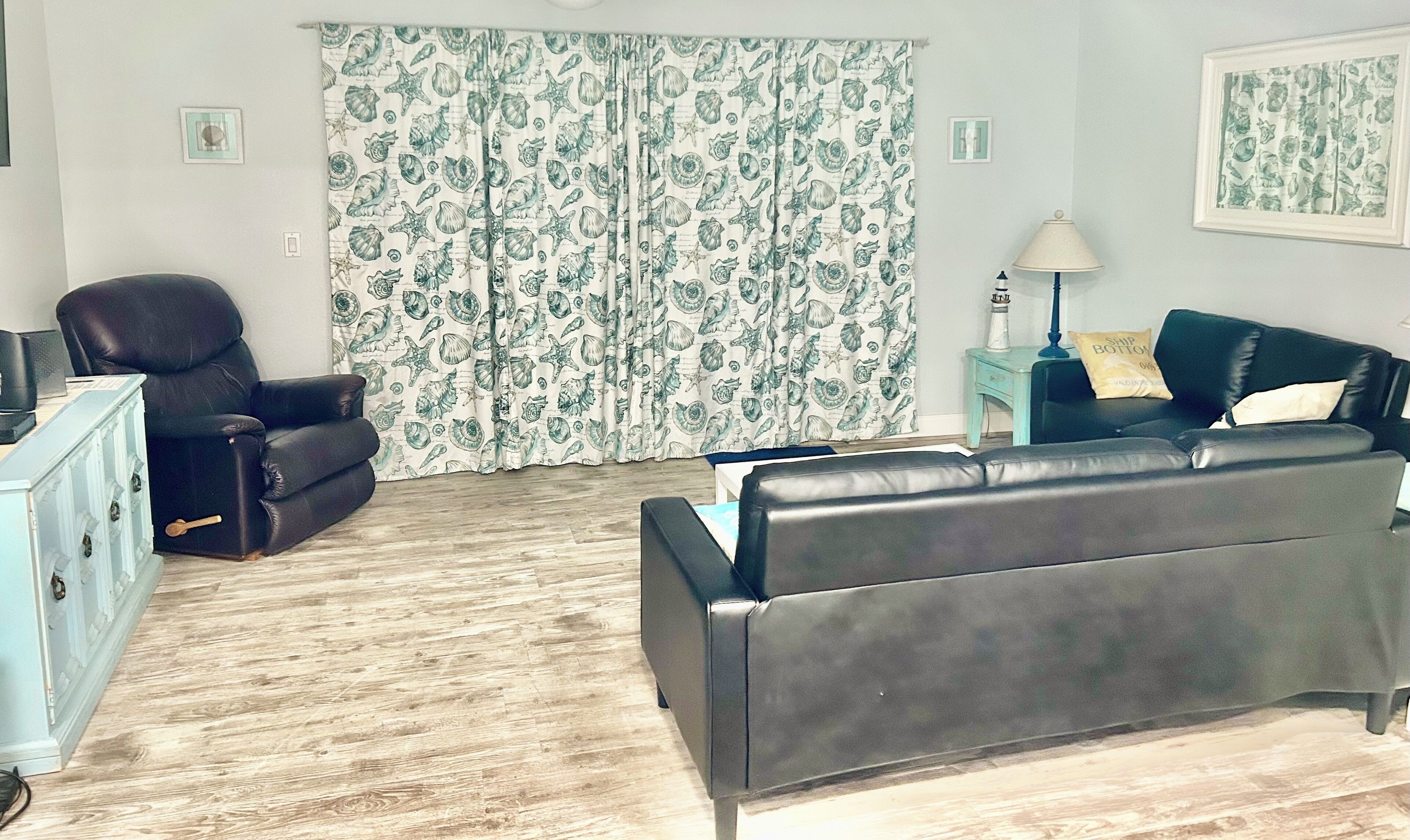 Ein Wohnzimmer mit einer schwarzen Ledersofa, einem schwarzen Sessel, einem kleinen Tisch mit einer Lampe und einem blauen Schrank.