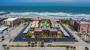 Ein Luftbild eines Hotels mit Parkplatz, Schwimmbad und Blick auf den Strand.
