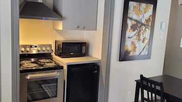 Cocina compacta con estufa, microondas y lavavajillas, una mesa de comedor con sillas y un cuadro en la pared.