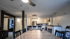 A spacious dining area with a long wooden table, black chairs, and a modern kitchen in the background.