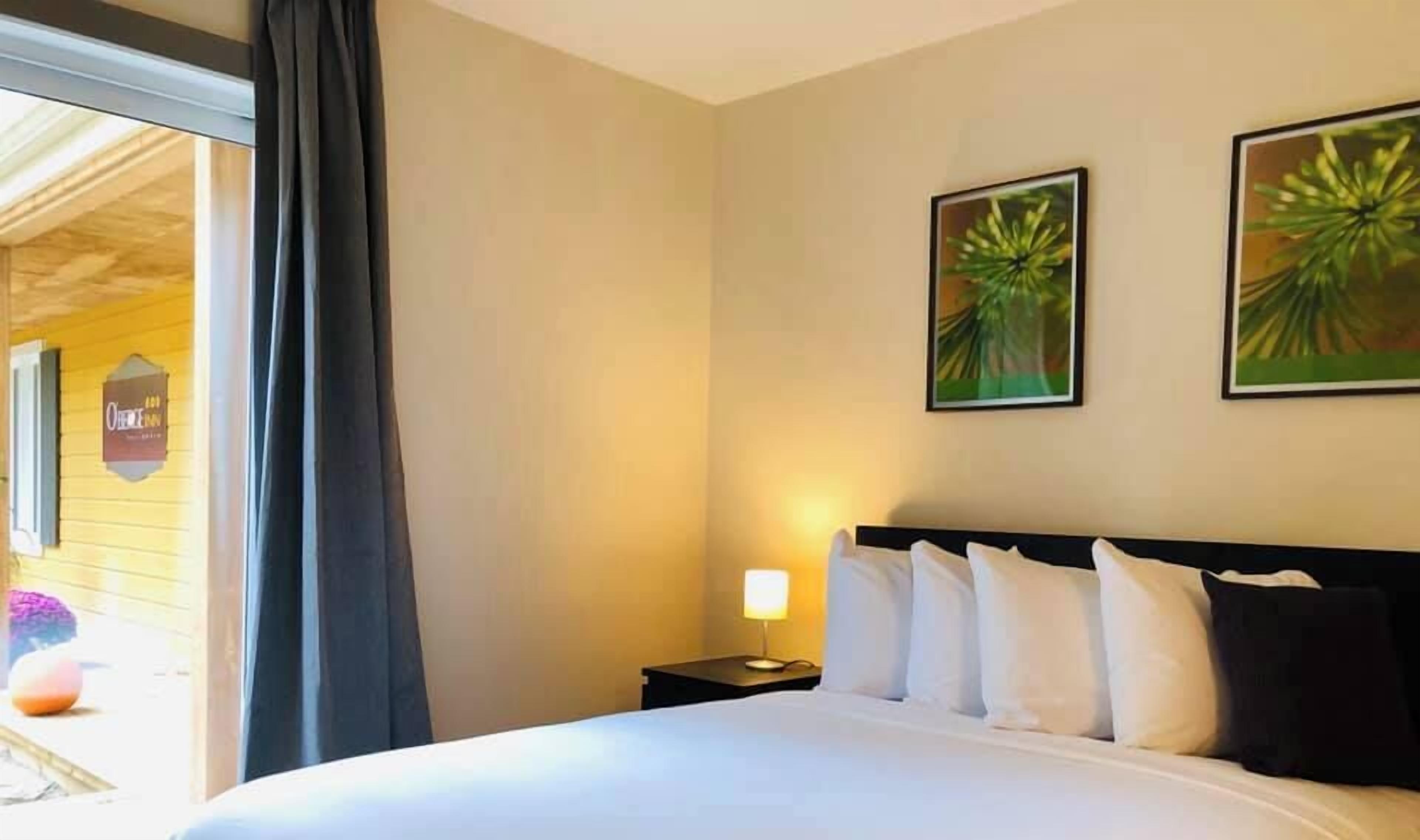 A hotel room with a bed, a nightstand with a lamp, and two framed pictures on the wall.