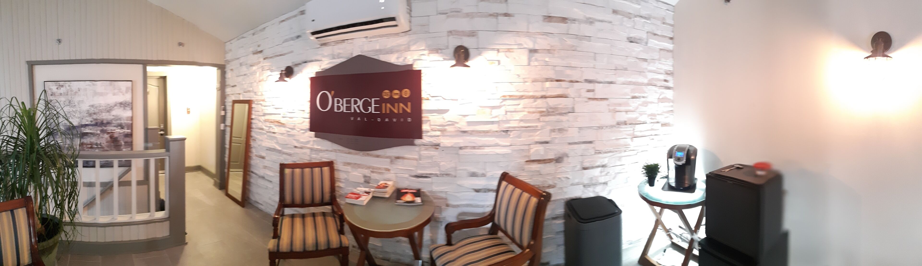 Un vestíbulo de hotel con una pared de piedra, un letrero que dice "O'Berge Inn" y una zona de estar con sillas y una mesa.