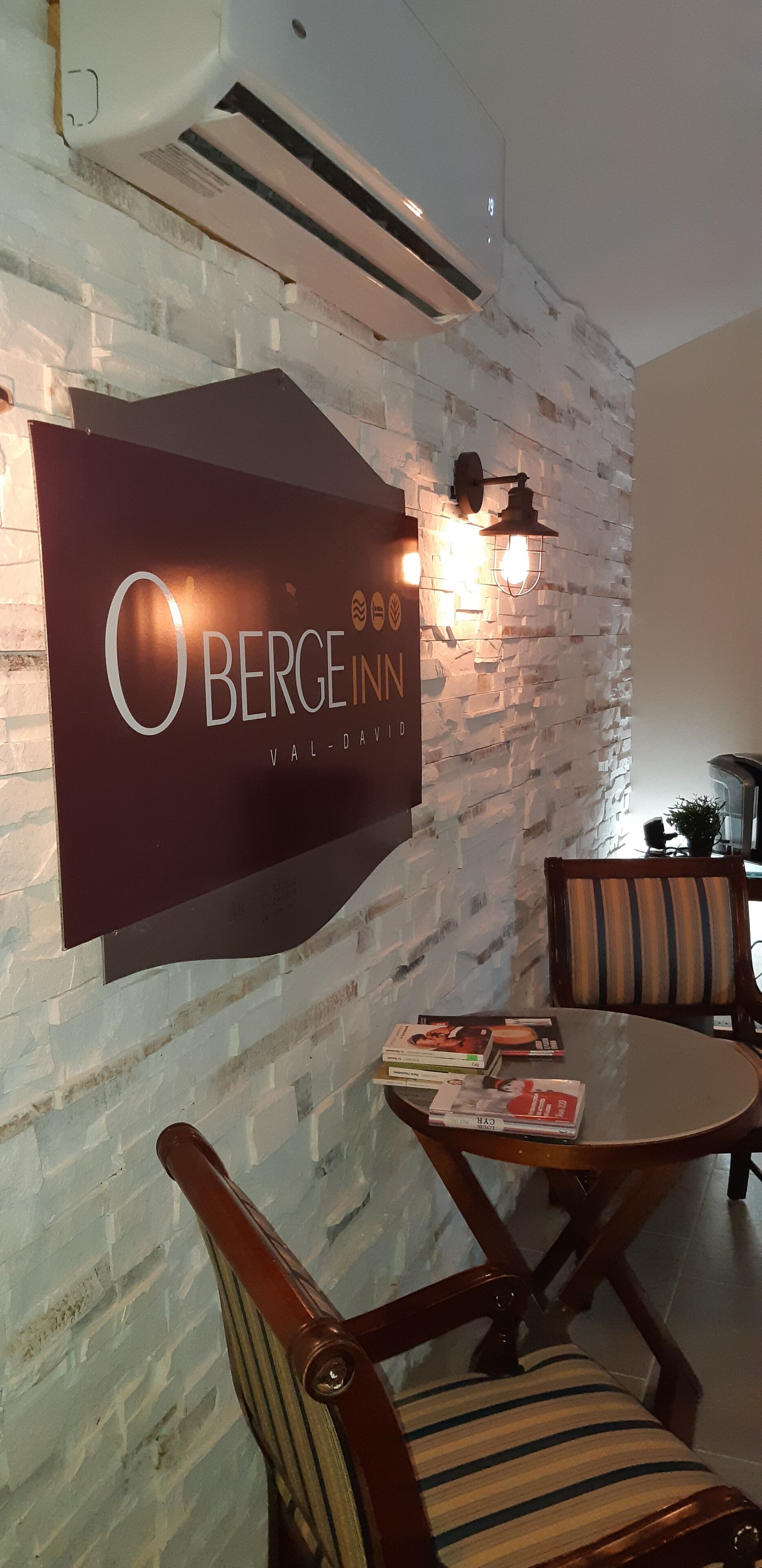 Un espace repas avec une table et des chaises, un panneau mural indiquant « Berge Inn Val-Davi », et un appareil de climatisation.