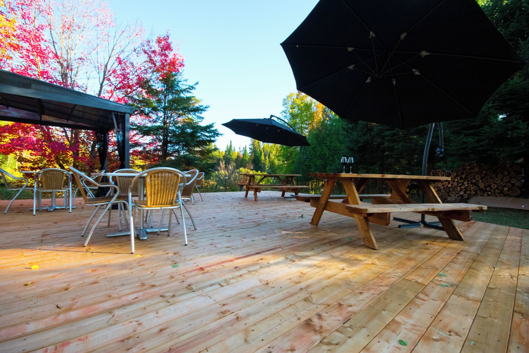 An outdoor patio with wooden tables and chairs, picnic tables, and a large umbrella.