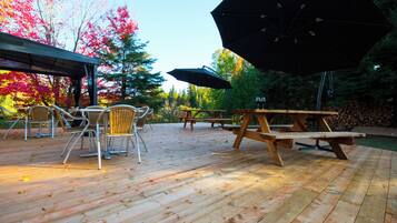 An outdoor patio with wooden tables and chairs, picnic tables, and a large umbrella.
