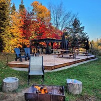 Una terraza exterior con mobiliario y una chimenea, rodeada de follaje otoñal.