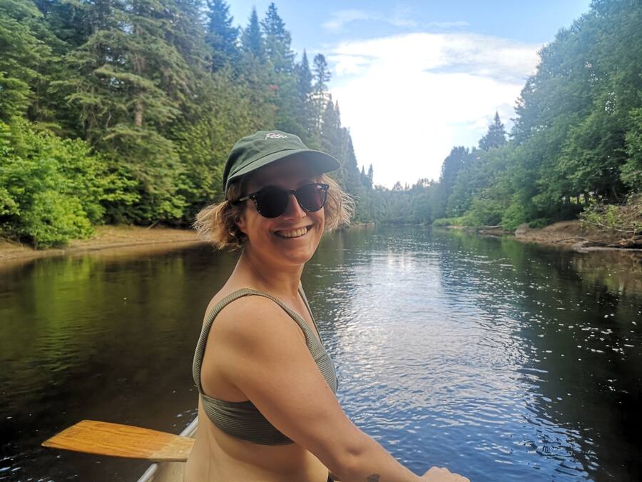 Une personne se trouve sur un bateau dans une rivière, entourée d’une forêt dense.
