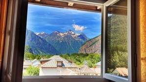 A window with a view of a mountain range and residential buildings. - Hotel Oberland (Le Bourg-d'Oisans)