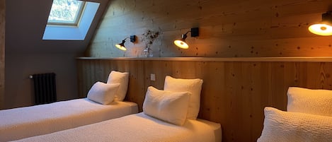 A room with two beds, wooden walls, a skylight, and wall-mounted lamps.