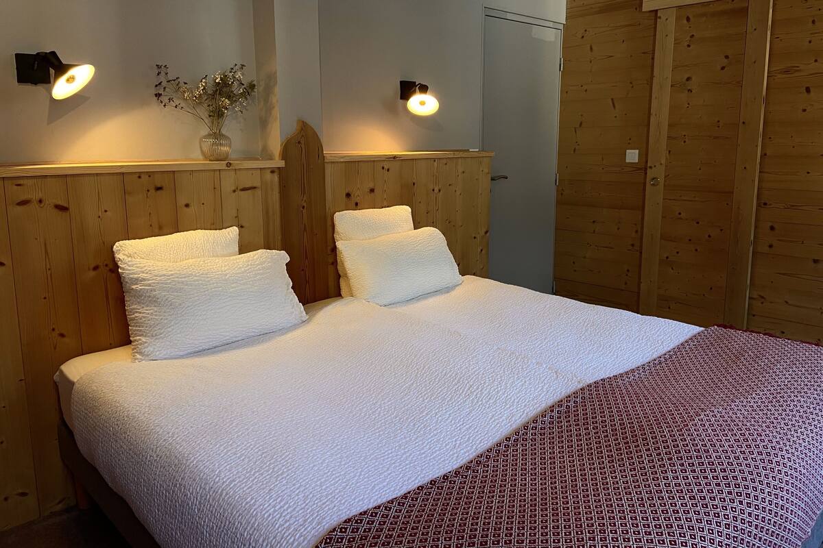 A bed with white bedding and two pillows, a wooden headboard, and two wall-mounted lights.