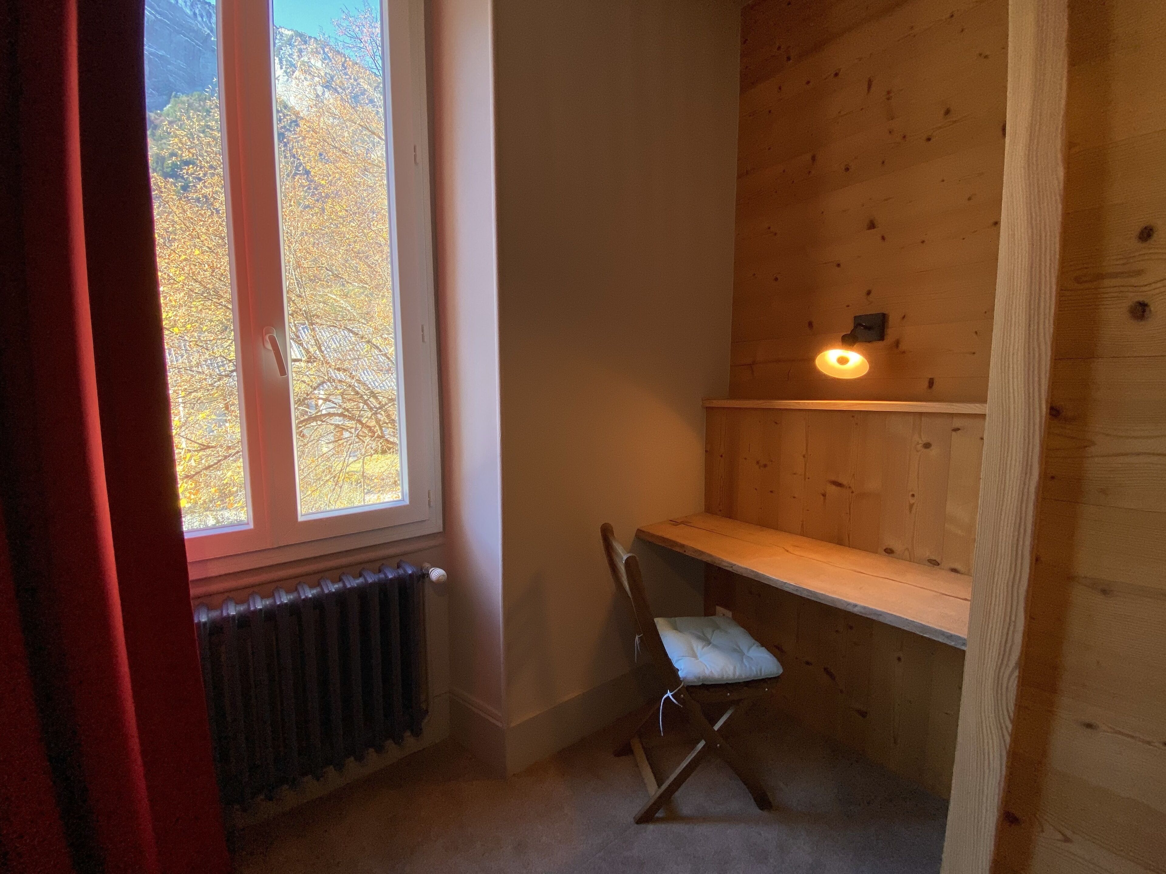 A small room with a window, radiator, wooden chair, and a shelf.