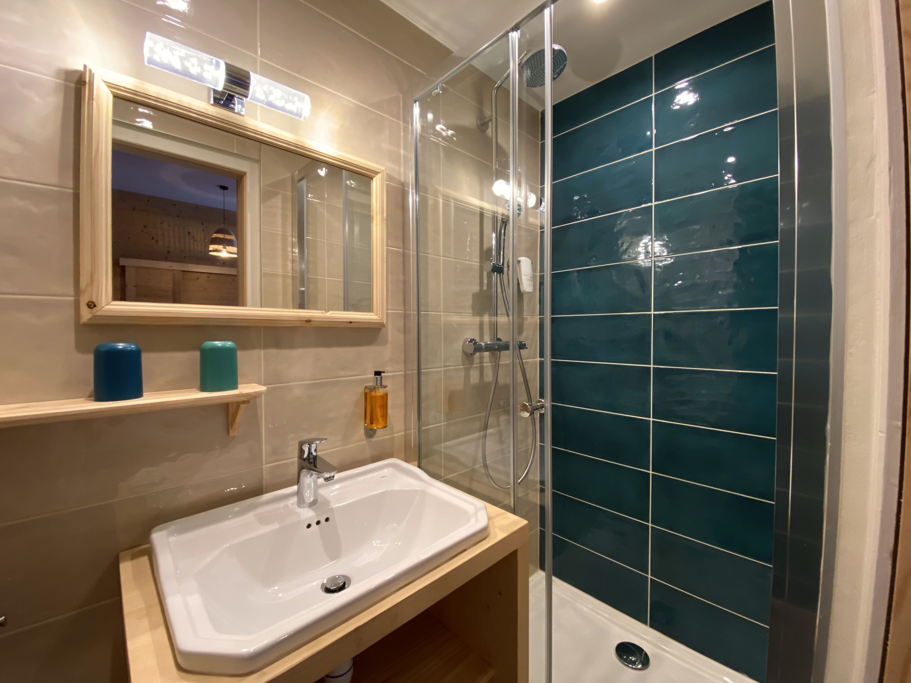 A bathroom with a glass-enclosed shower, a white sink, a mirror, and a shelf with toiletries.