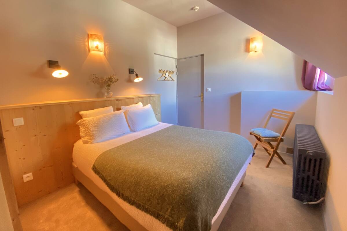A bedroom with a bed, a chair, a radiator, and wall-mounted lights.