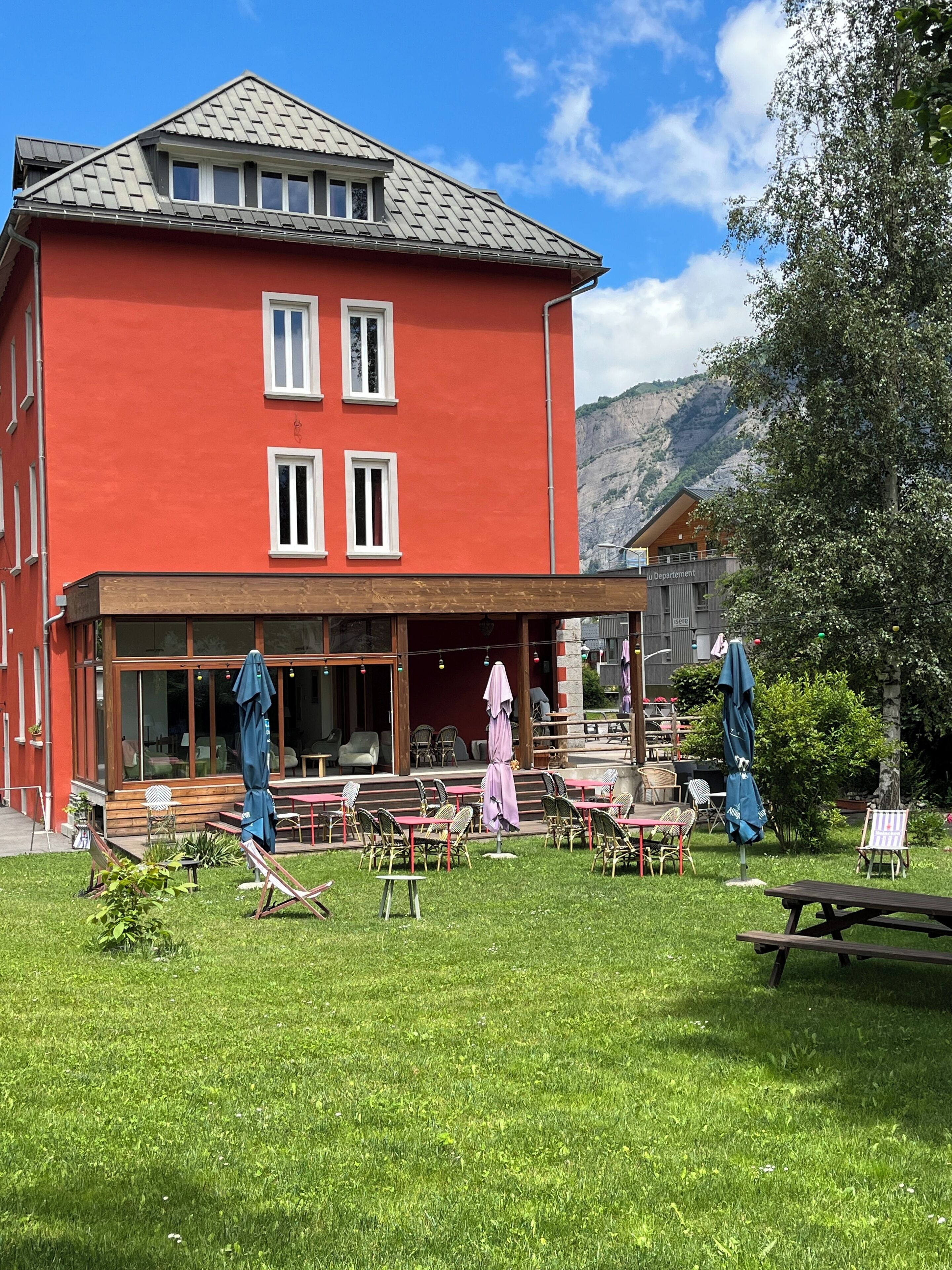 A red building with a covered outdoor seating area, tables, and chairs.