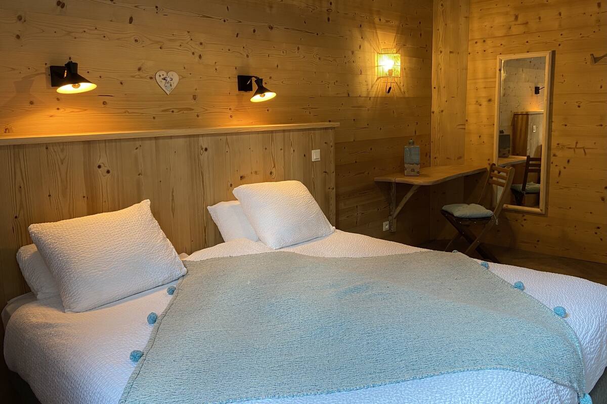 A wooden cabin room with a bed, two wall-mounted lights, a mirror, and a small table.