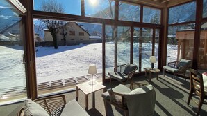 A sunlit room with large windows, wicker furniture, and a view of a snowy landscape. - Hotel Oberland (Le Bourg-d'Oisans)