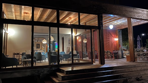 A restaurant with a wooden exterior and large windows. Inside, there are multiple tables and chairs arranged for dining. - Hotel Oberland (Le Bourg-d'Oisans)