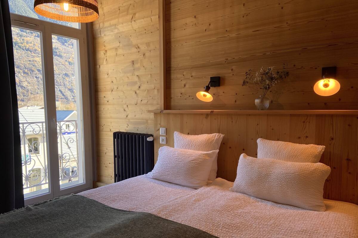 A wooden-paneled room with a bed, two wall-mounted lights, and a view through a glass door.