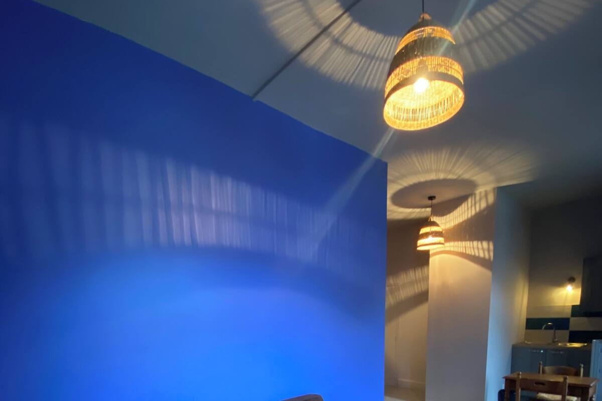 A room with a blue wall, a brown sofa, a round wooden table, and a hanging light fixture.