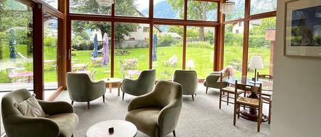 A spacious room with large windows, comfortable seating, and a view of a lush garden.