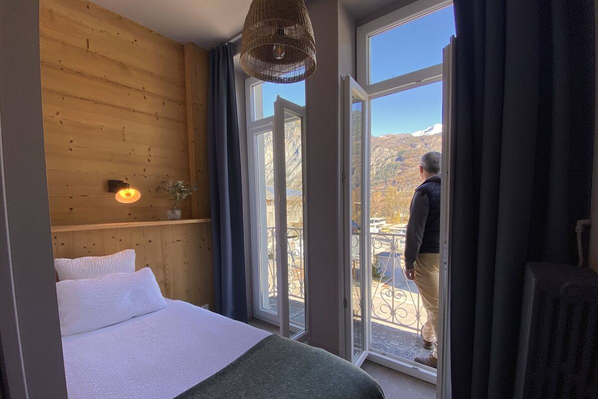 A bedroom with a large bed, wooden walls, a window, and a view of a mountain.
