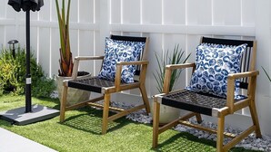 Zwei Holzstühle mit blauen Kissen, ein schwarzer Sonnenschirm und ein weißer Zaun in einem Garten.