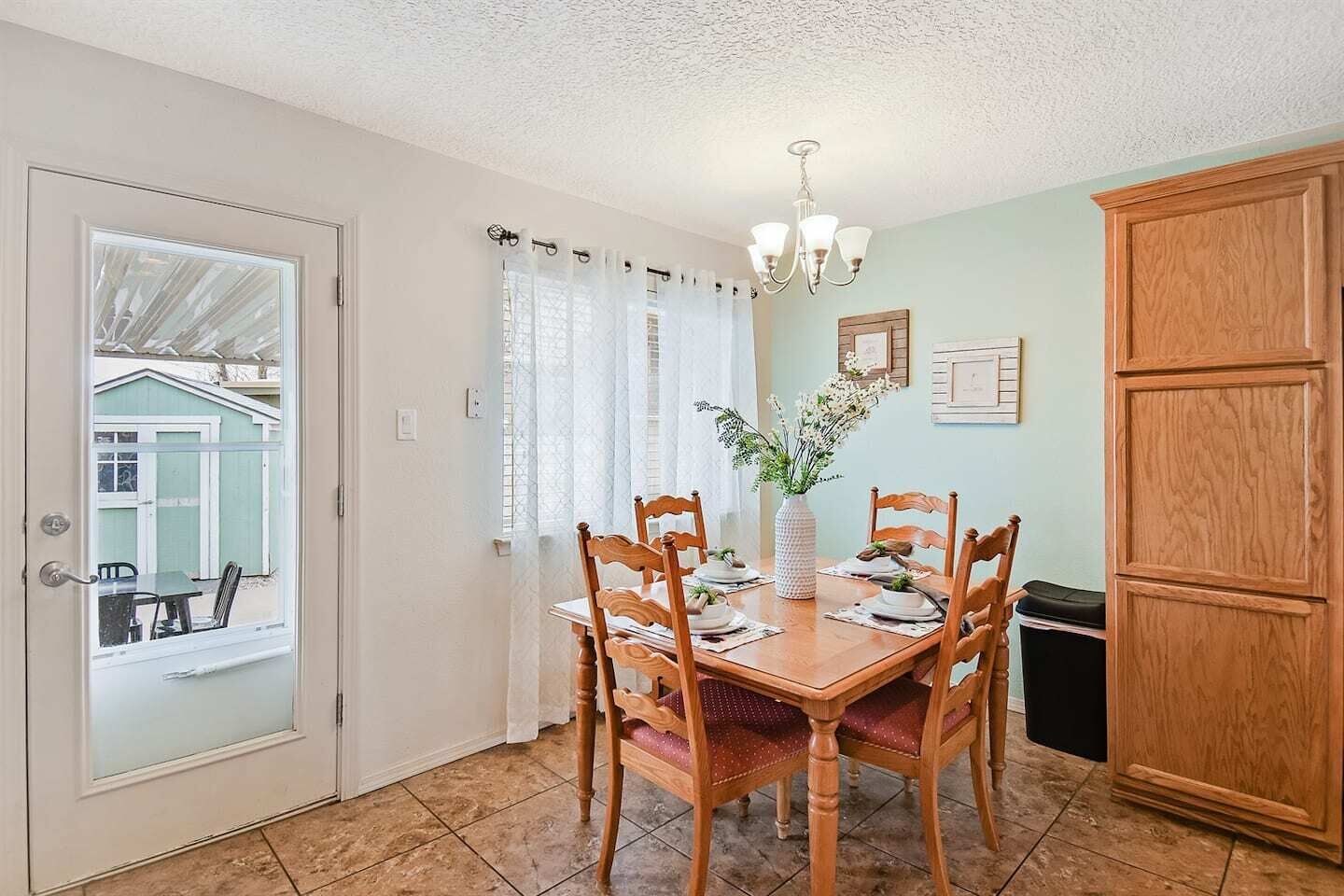 A dining area with a wooden table and chairs, a vase with flowers, and a view through a glass door to an outdoor area.