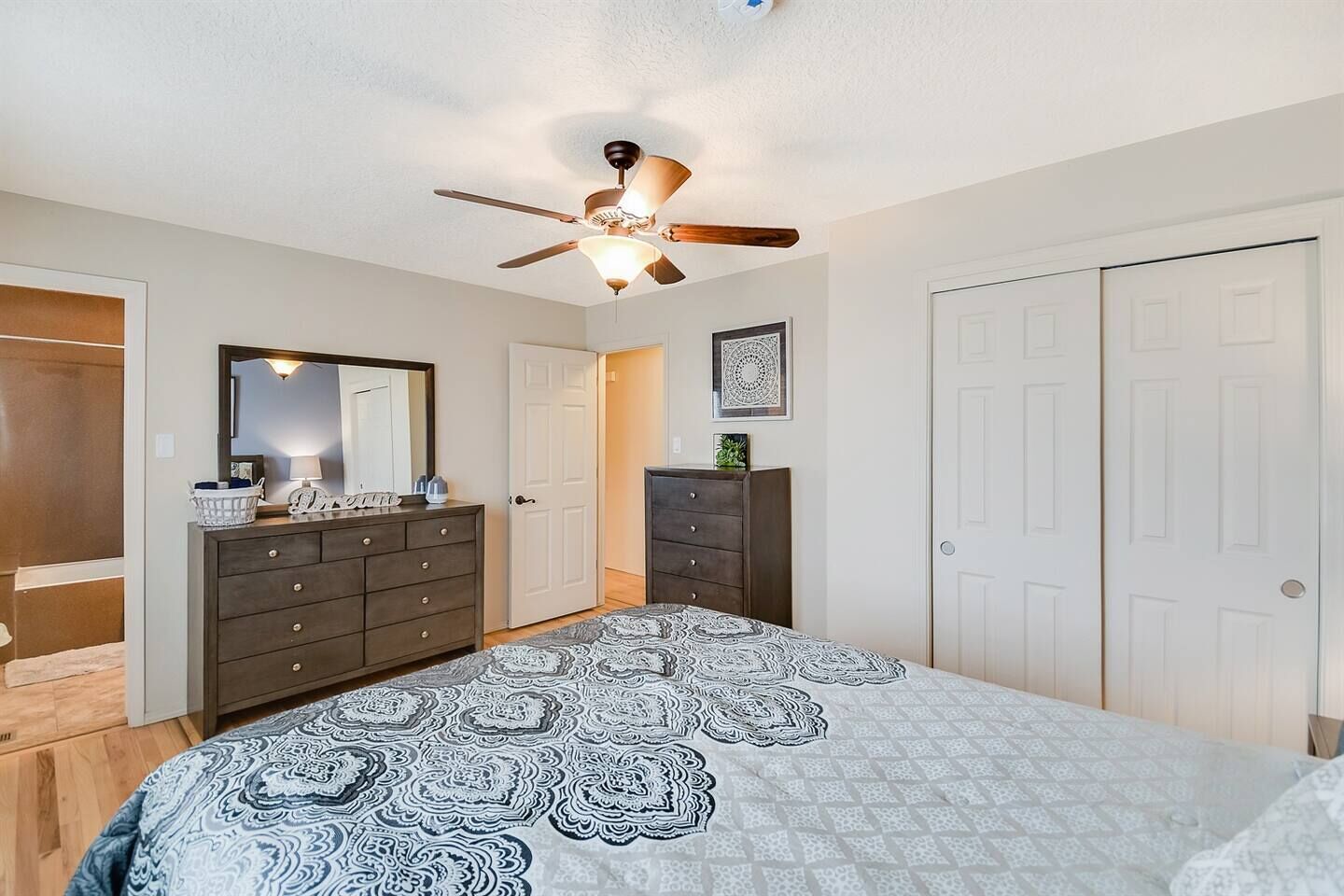A bedroom with a bed, a dresser, a ceiling fan, and a door.
