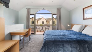 Une chambre d’hôtel équipée d’un lit, d’un bureau, d’une chaise et d’un balcon donnant sur des immeubles.