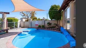 Une piscine avec une terrasse en bois, un espace ombragé et une vue sur un quartier résidentiel.