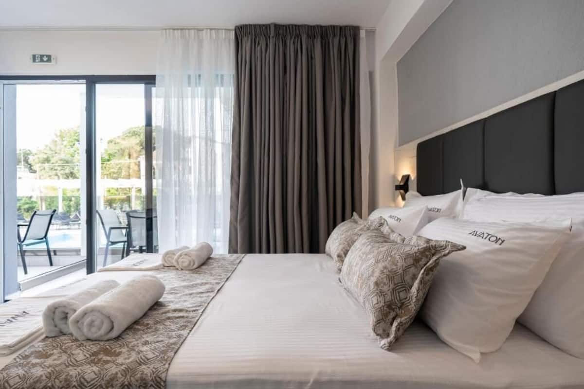 A hotel room with a bed, pillows, a view of the outdoors, and a window with curtains.