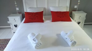 A hotel room with a large bed, two red pillows, white nightstands, and two rolled towels. - House with bay view in the heart of the city (Saint-Valery-sur-Somme)