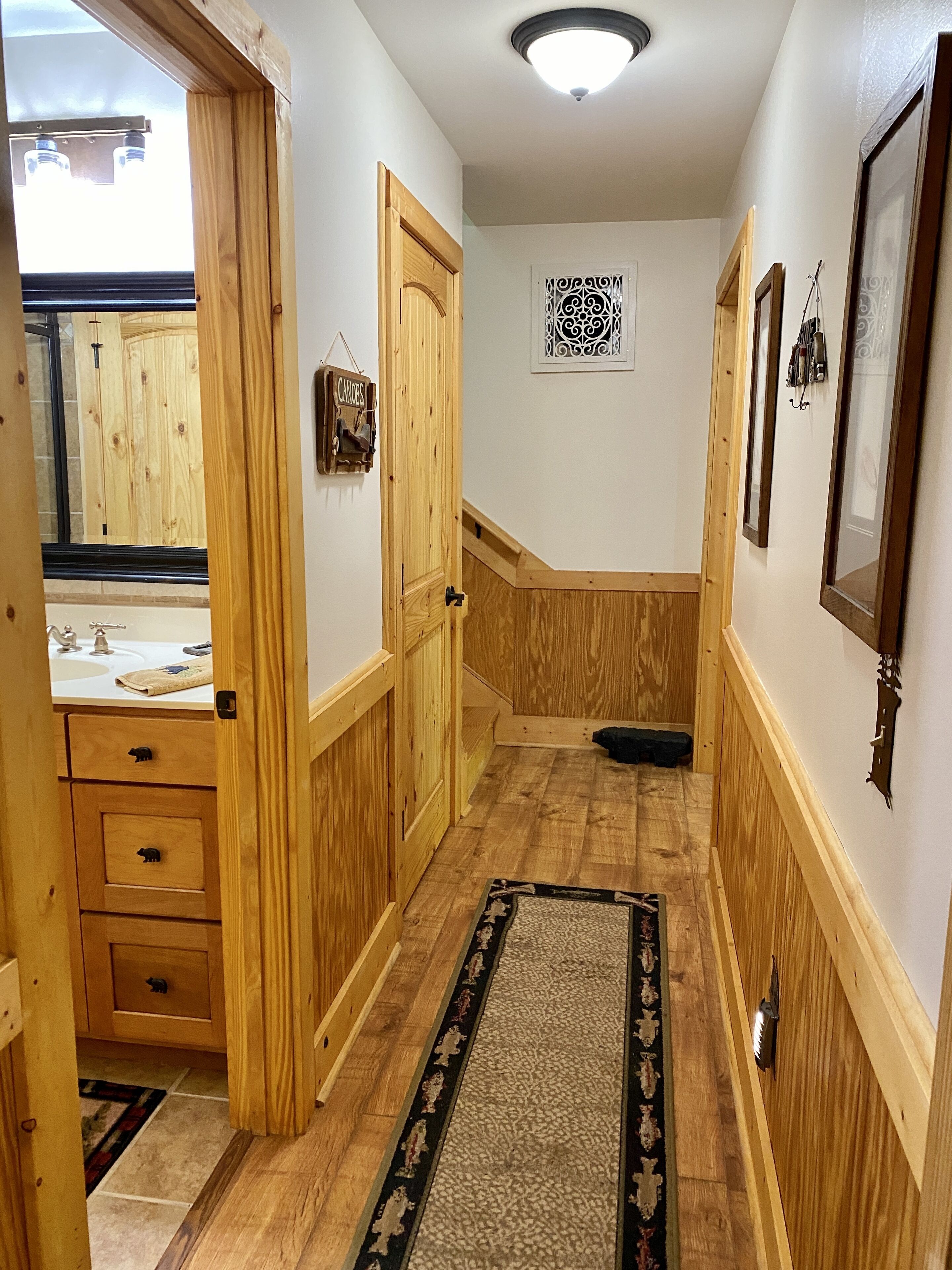 Ein Korridor mit Holzwandverkleidung, einem Teppich, einem Waschbecken und einem gerahmten Bild an der Wand.