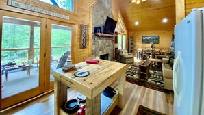 A cozy cabin interior with a stone fireplace, wooden walls, and a dining area. - Riverfront Cabin Downtown Helen! Hot Tub, FirePit,Arcade,Tubing & Private Park!♥️ (Helen)
