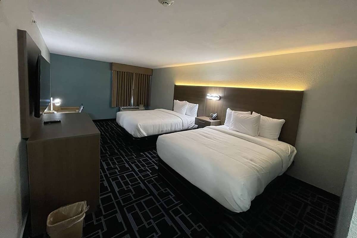 A hotel room with two beds, a desk, a mirror, and a trash bin.