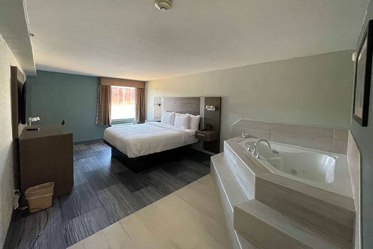 A hotel room with a large bed, a separate bathroom with a bathtub, a desk, and a chair.